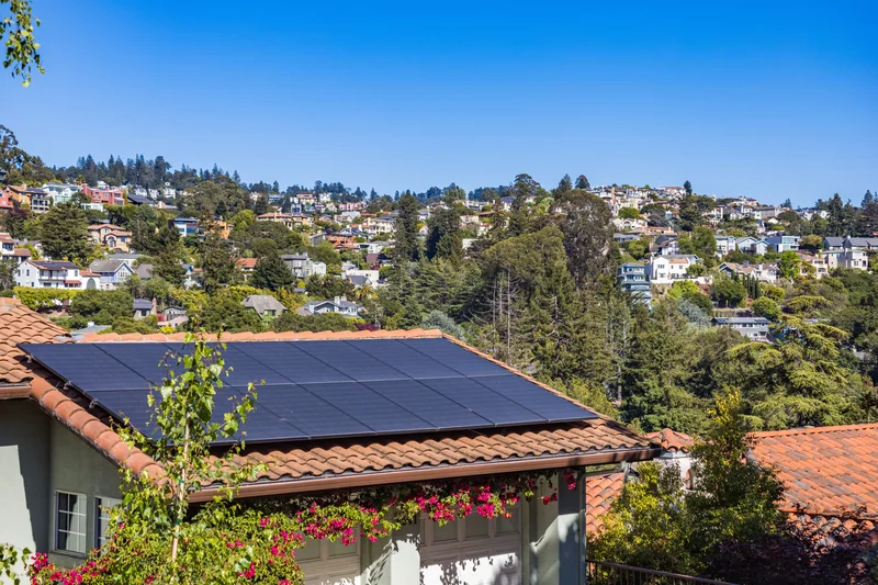 Solar panels on a tiled roof with flowers and a green hillside neighborhood